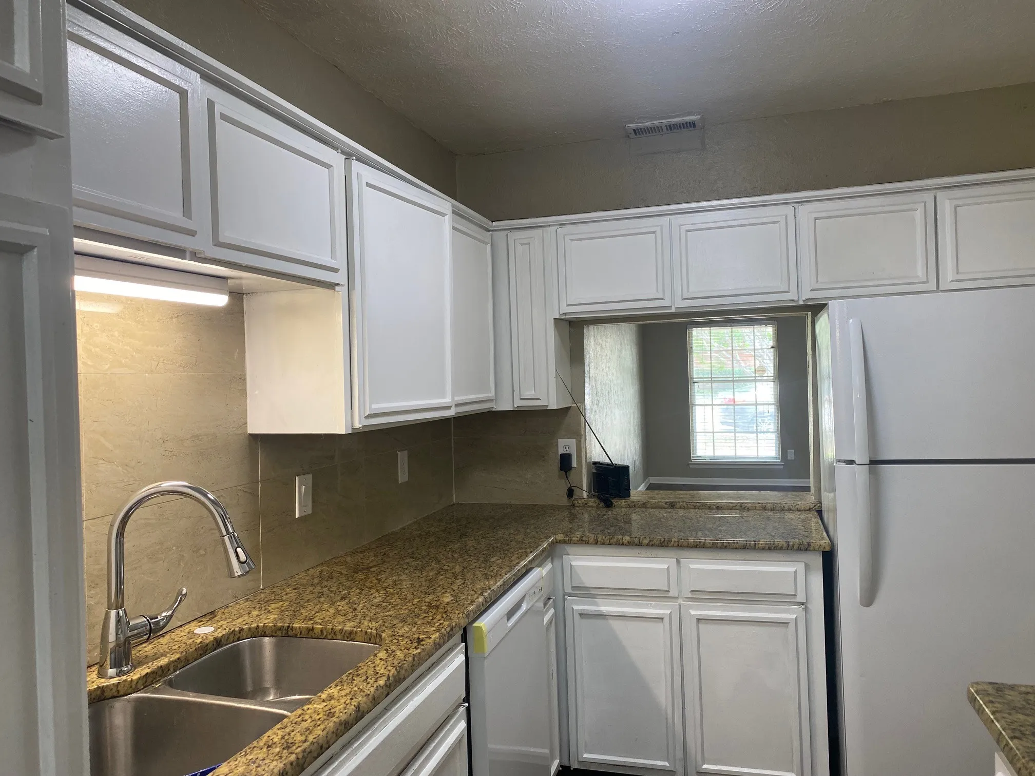 Kitchen featuring white appliances, decorative backsplash, white cabinetry, dark stone countertops, and a textured ceiling