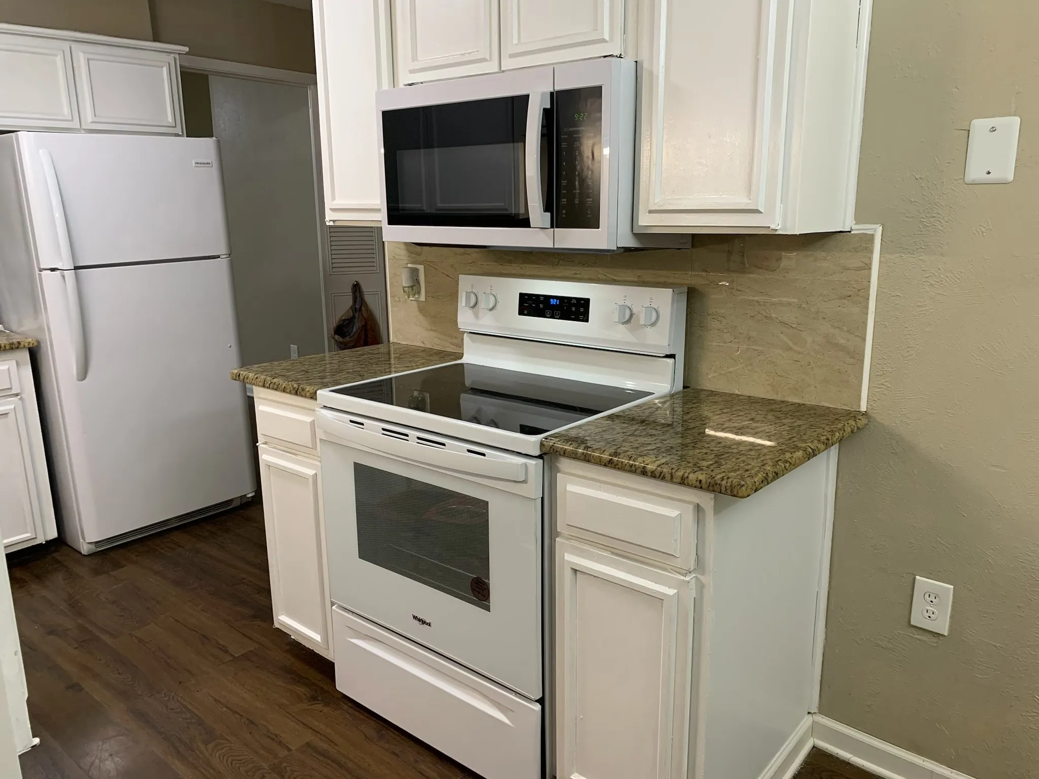 Kitchen featuring white cabinetry, granite countertops, tile backsplash, wood-finish flooring, and white appliances including a range and microwave
