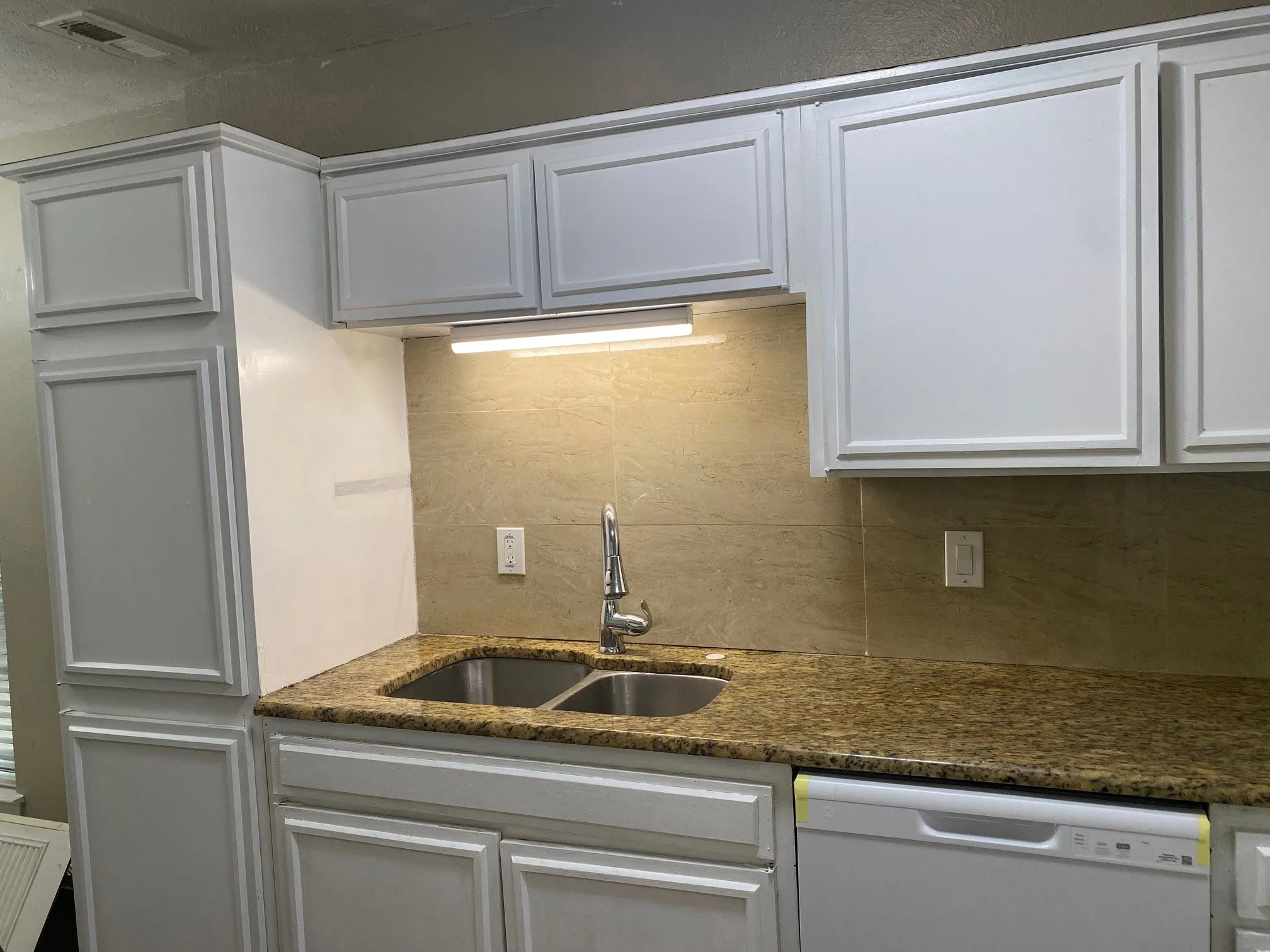 Kitchen with white dishwasher, white cabinetry, dark stone counters, and decorative backsplash