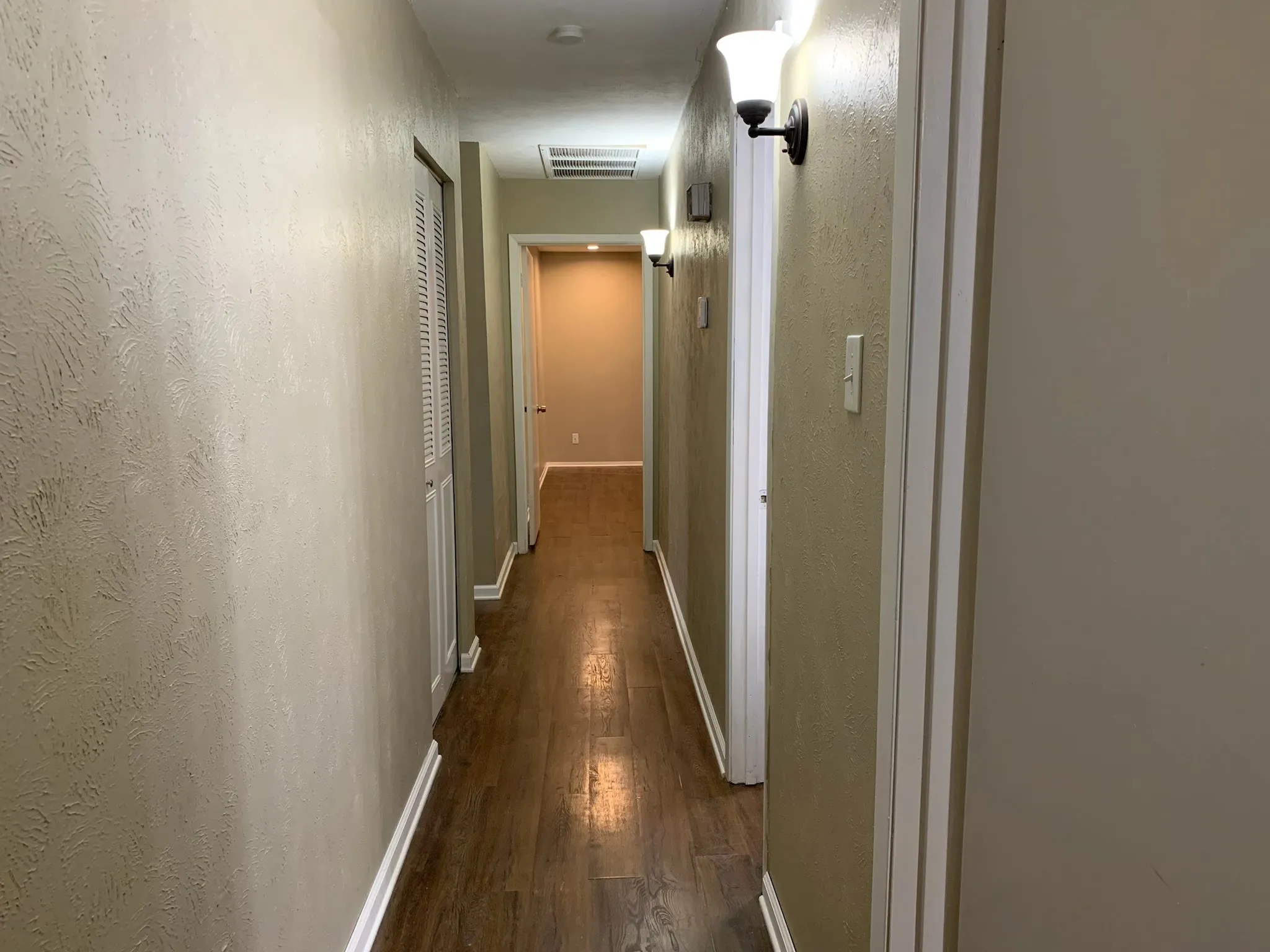 Corridor with dark wood-type flooring and a textured wall
