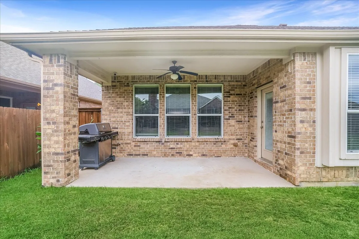 Covered patio featuring a ceiling fan, brick pillars, a concrete slab, and a glass-paneled door