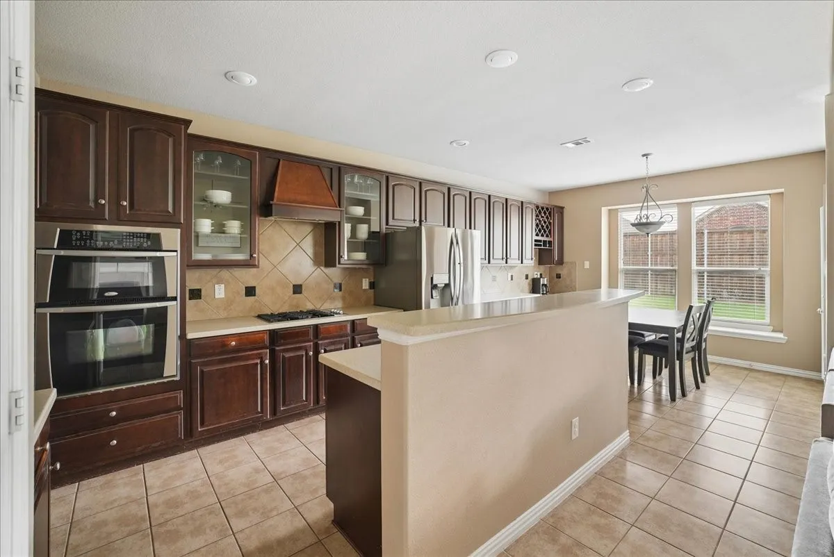 Kitchen featuring dark wood cabinetry, stainless steel double ovens, a built-in gas cooktop, and light-colored countertops