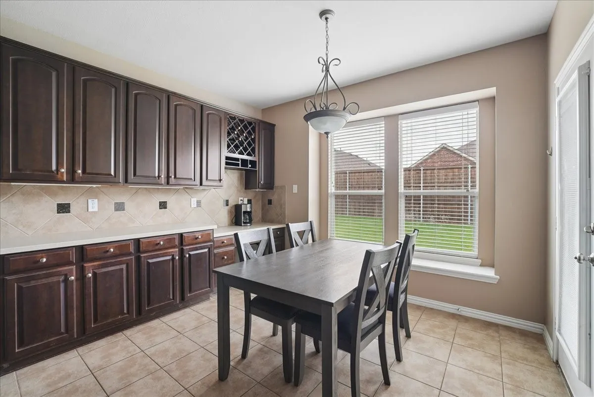 Kitchen dining area featuring extensive dark wood cabinetry, light countertops, and a tiled backsplash with decorative accents