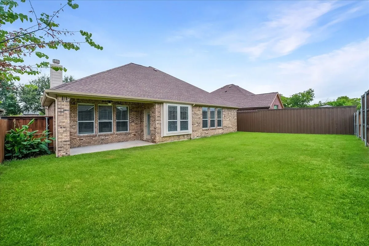 Expansive grassy yard featuring a covered patio, brick exterior, multiple windows, and a privacy fence