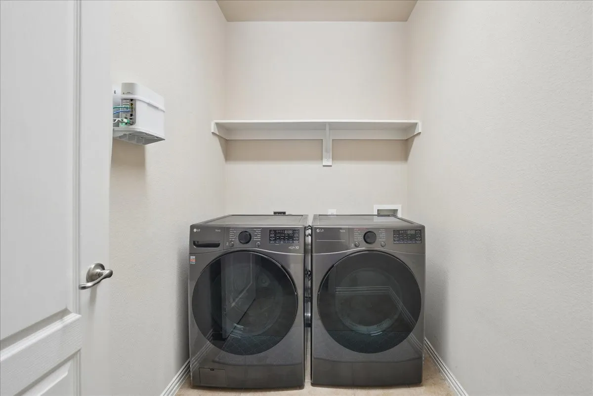 Dedicated utility space featuring light-toned walls, a built-in wall shelf, and wood-finish flooring