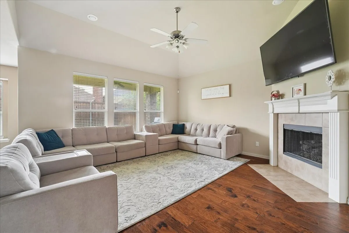 Spacious living area featuring high vaulted ceilings, rich wood-finish flooring, and a fireplace with a tiled hearth and mantel