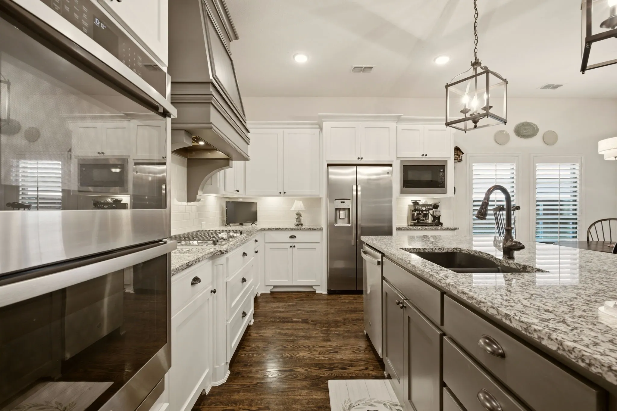 The upgraded kitchen package includes stainless appliances--a 36" wide GE 5-burner gas cooktop, double ovens, dishwasher & room for your own refrigerator. Note the custom-color range hood & matching tone island with granite countertops & pendant lights above. Cabinet hardware added too.