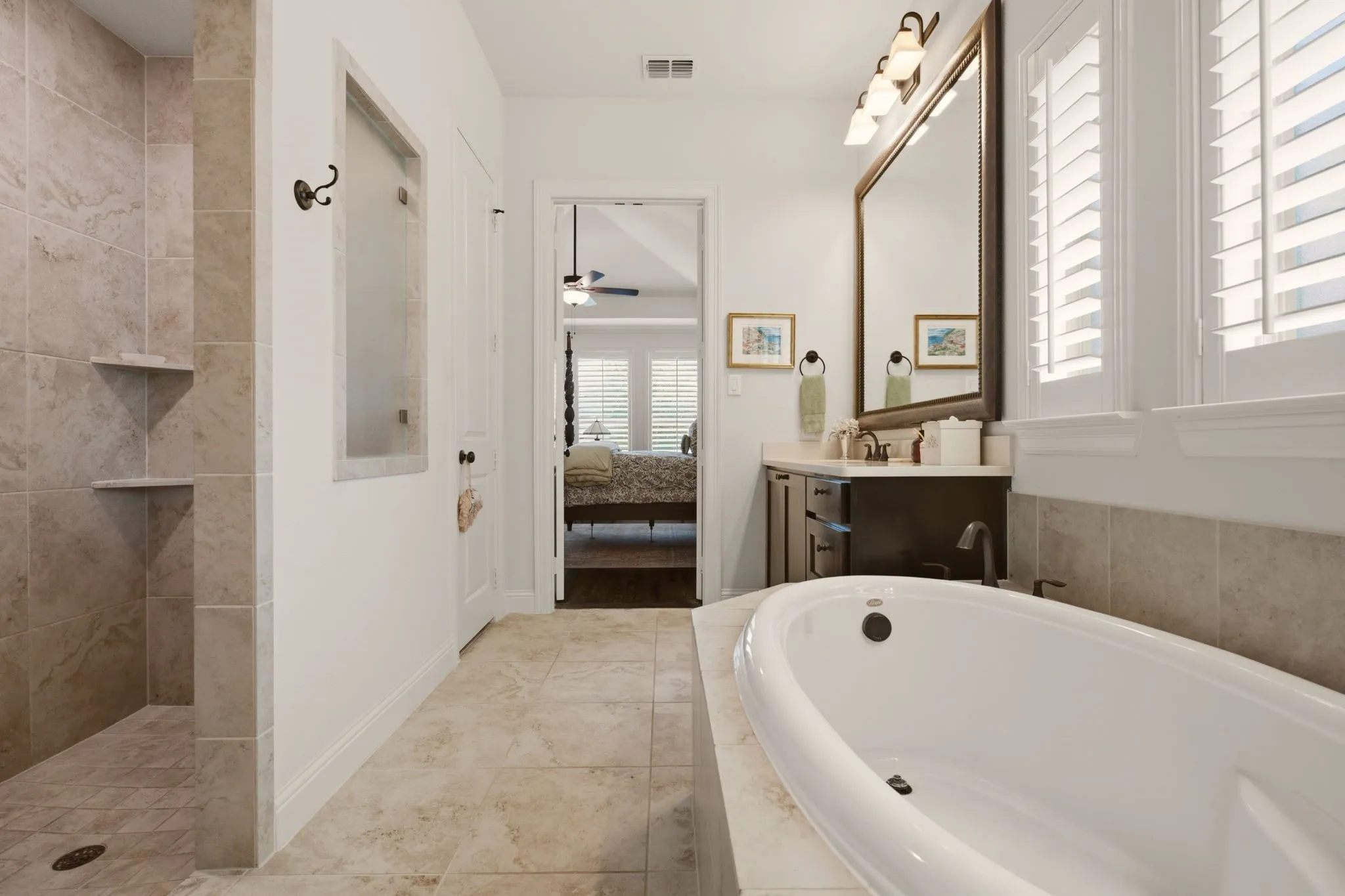 This pristine primary bathroom has a deep walk-in tiled shower & custom-framed mirrors.