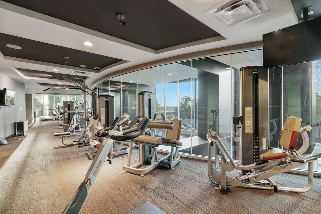 Fitness center featuring a variety of exercise equipment, carpet flooring, a drop ceiling with recessed lighting, and expansive windows