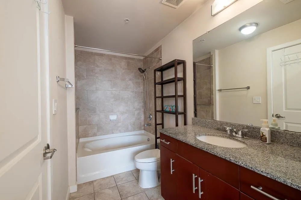 Bathroom featuring a granite countertop vanity with an undermount sink, cherry wood-finish cabinetry, and a full bathtub with subway tile surround