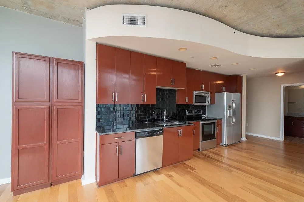 Kitchen featuring finish flooring, dark subway tile backsplash, stainless steel appliances, and abundant cabinetry