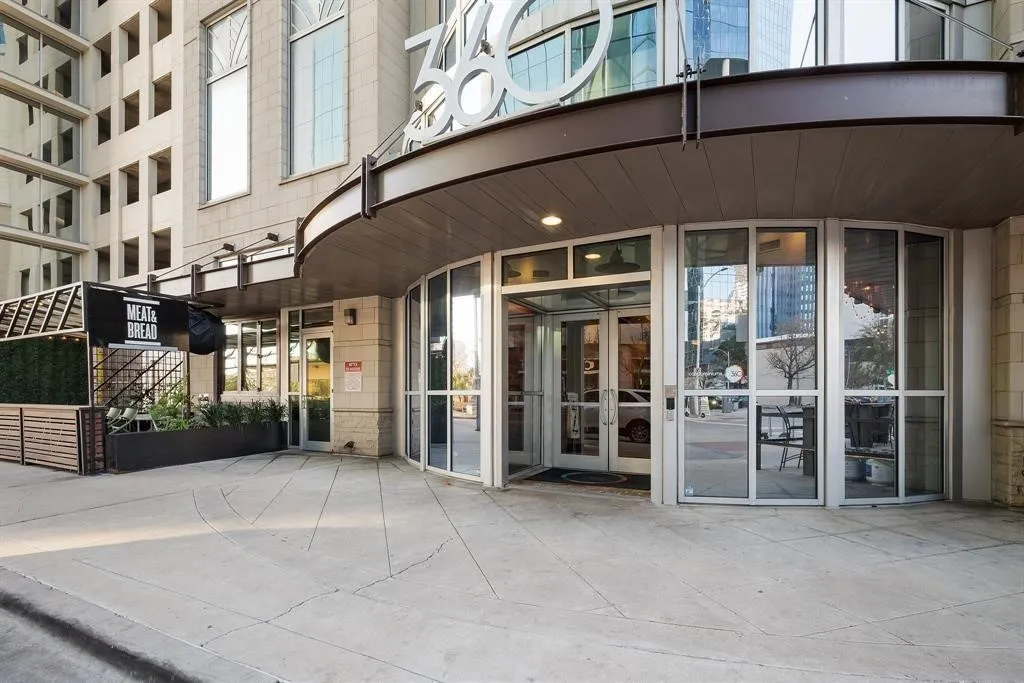Modern commercial building entrance with a curved awning, full-height glass doors, and an integrated exterior dining area