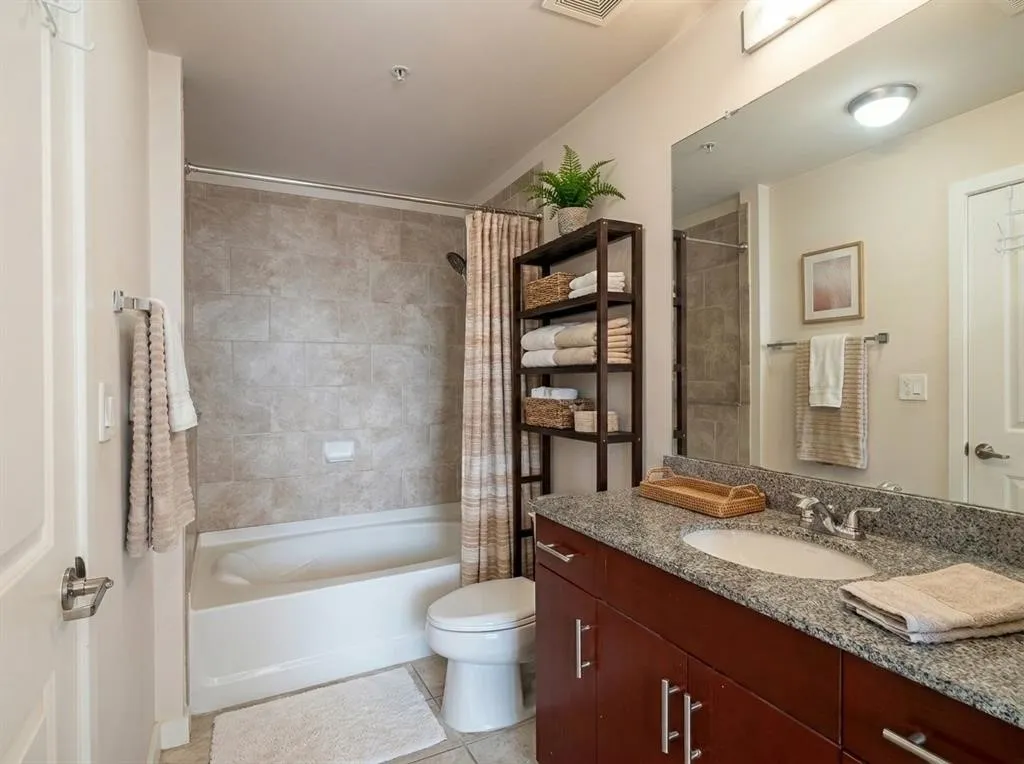 Bathroom featuring a built-in bathtub with subway tile surround, granite countertop vanity, wood-finish cabinetry, and recessed lighting Virtually Staged