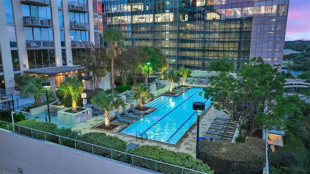 Rooftop amenity deck featuring a lap pool with integrated lighting, surrounding paved patio, and mature palm trees
