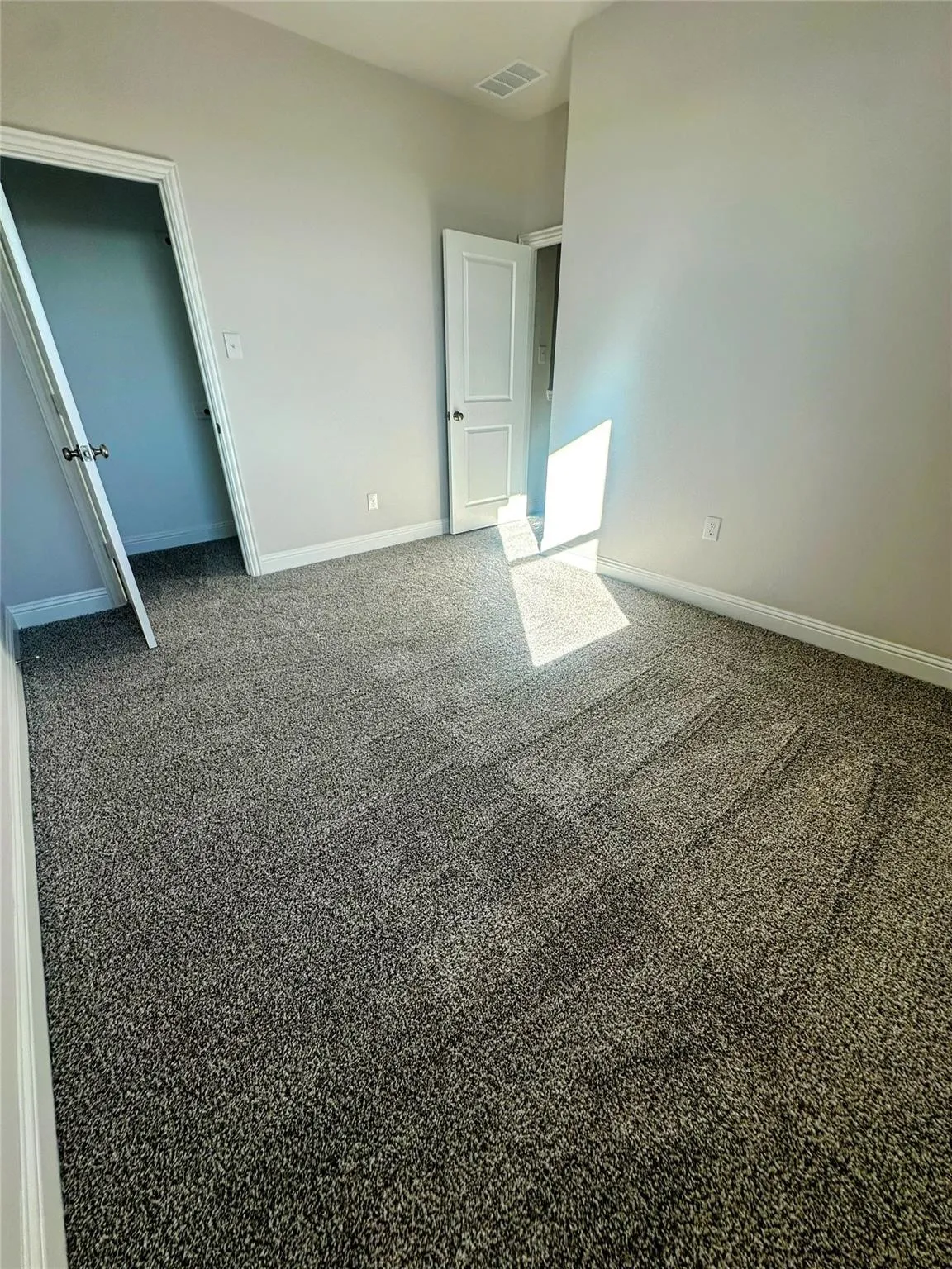 Room featuring neutral wall paint, gray textured carpet, white baseboards, and white two-panel doors