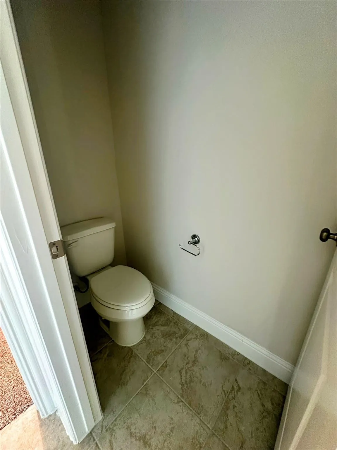 Powder room featuring a two-piece toilet, ceramic tile flooring, neutral wall tones, and a chrome toilet paper holder
