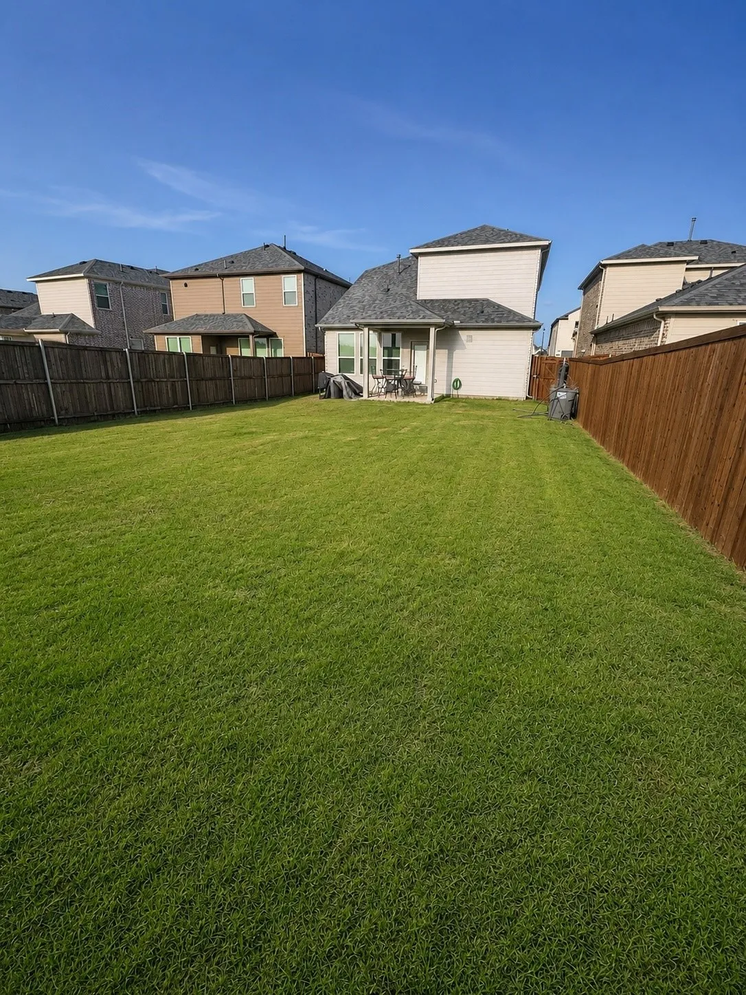 Expansive rear yard featuring a large green lawn, a covered patio, and privacy fencing