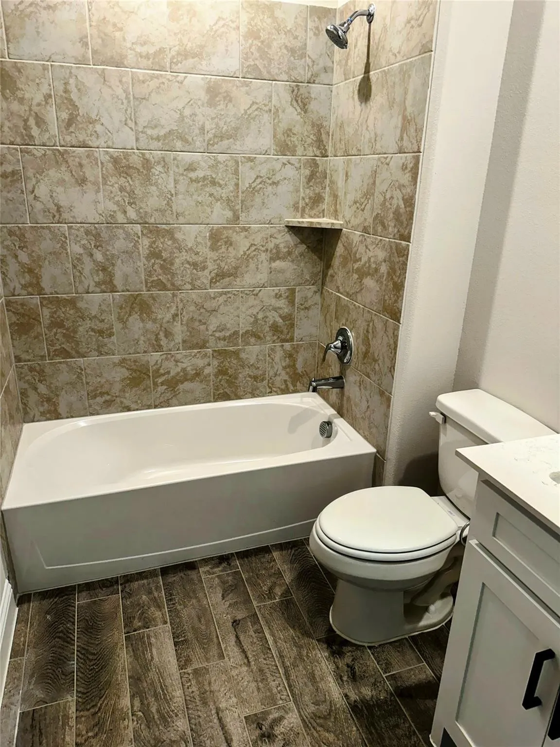 Bathroom featuring a white bathtub, ceramic tile surround with built-in shelf, and wood-finish flooring