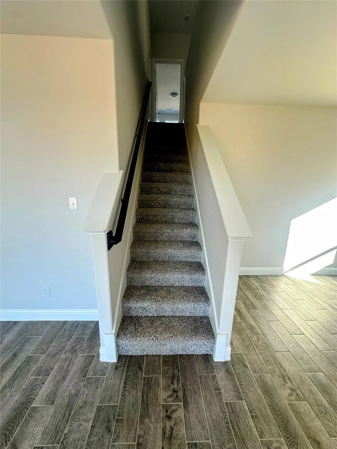 Carpeted staircase with white balustrades and a dark handrail, complemented by wood-look tile flooring