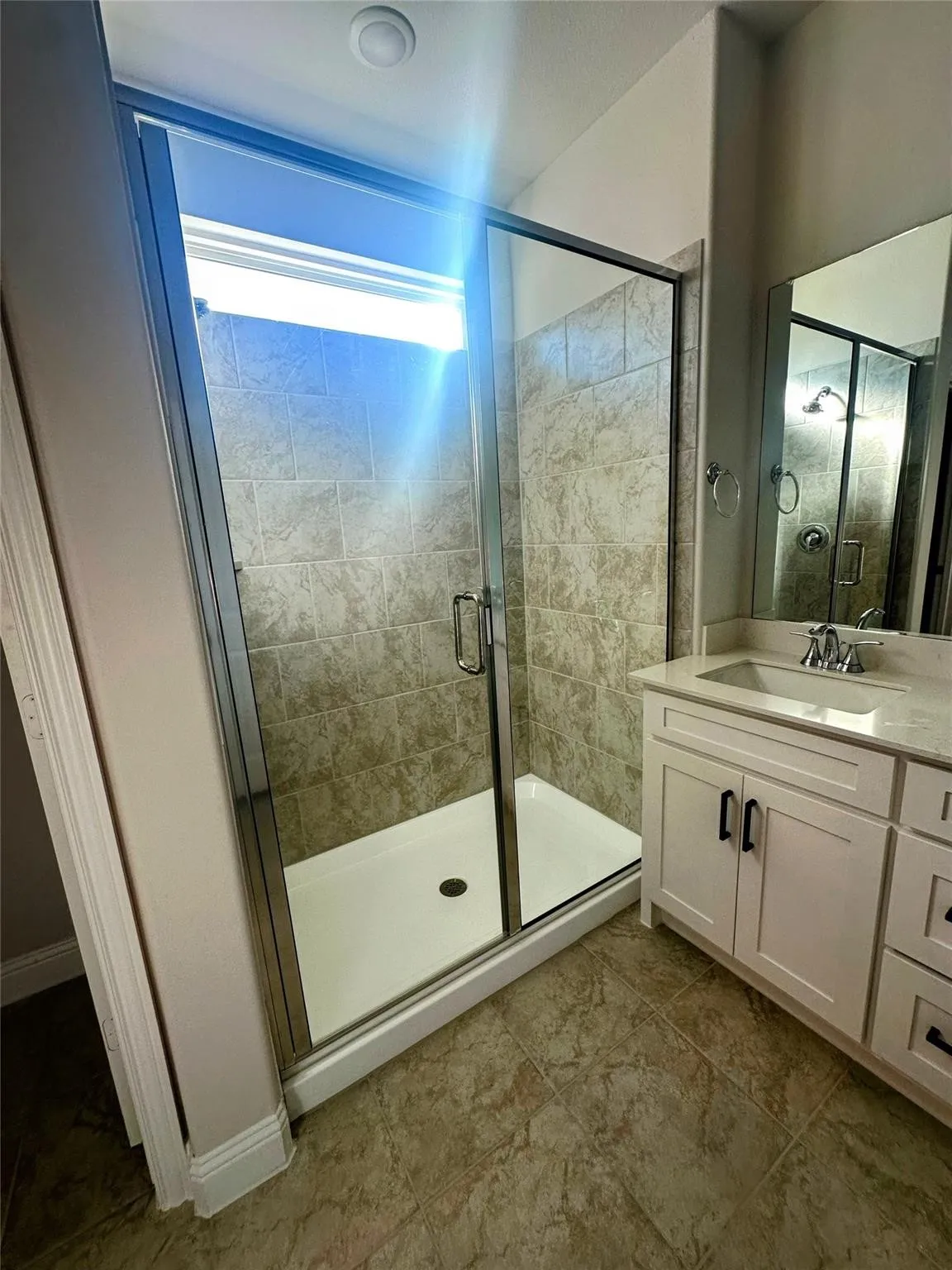 Contemporary bathroom featuring a glass-enclosed shower with tile surround, a white vanity with a light-toned countertop, and a large wall mirror