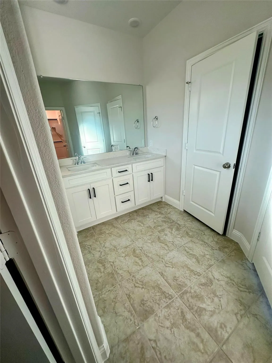 Double vanity with white cabinetry and black hardware, set against a full-width mirror