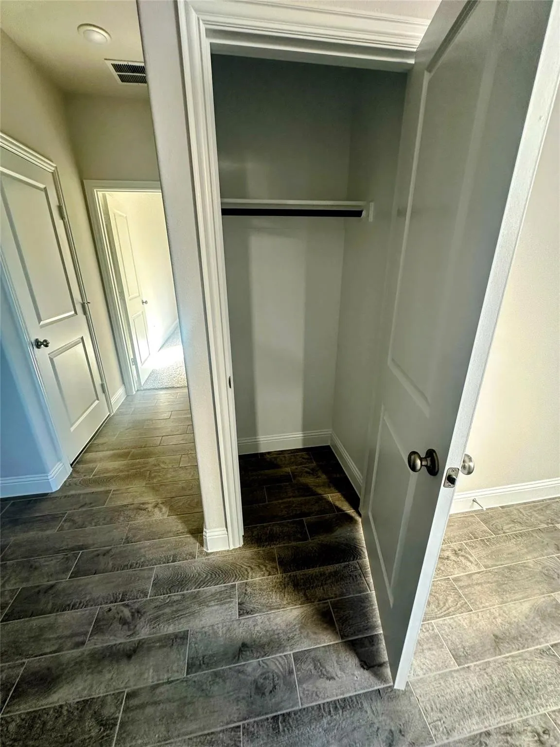 Entryway closet with a single hanging rod, featuring wood-finish tile flooring