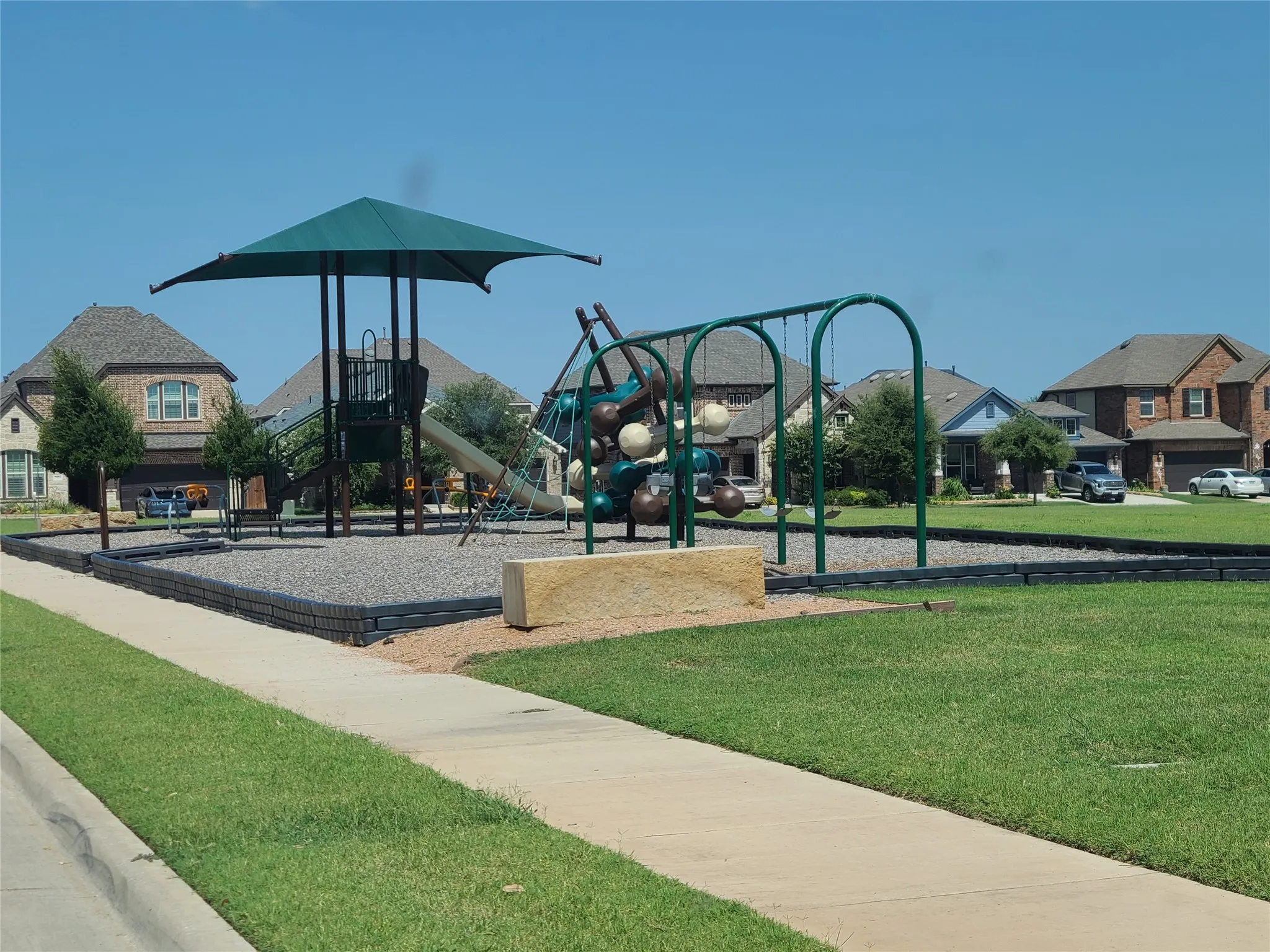 Community playground featuring a multi-level play structure with a shade canopy, slide, and climbing elements