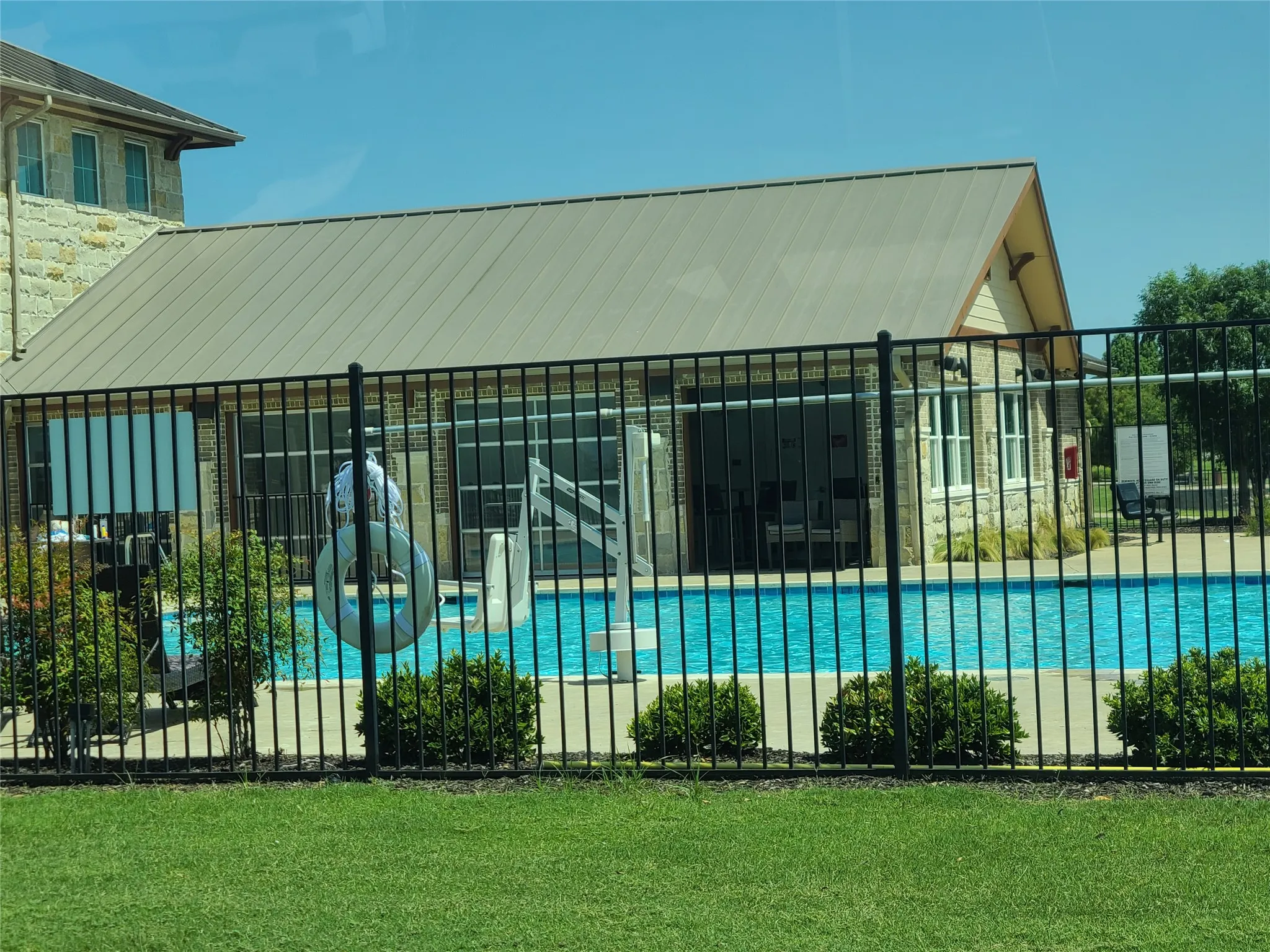 Fenced swimming pool with a stone and brick pool house featuring a metal roof and large glass paneled doors