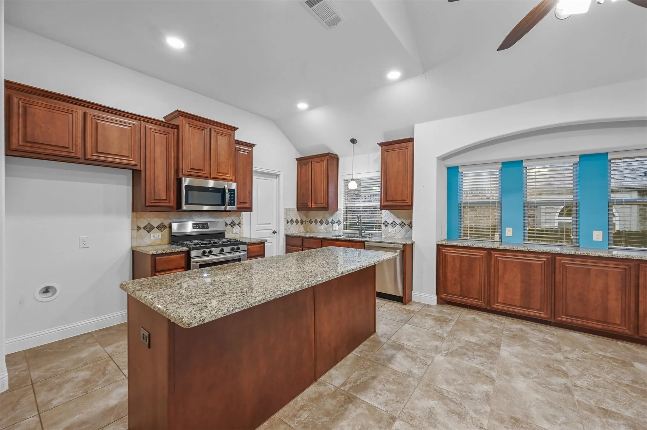 Kitchen featuring a central island with a light-toned countertop, wood-finish cabinetry, stainless steel appliances, and tile flooring