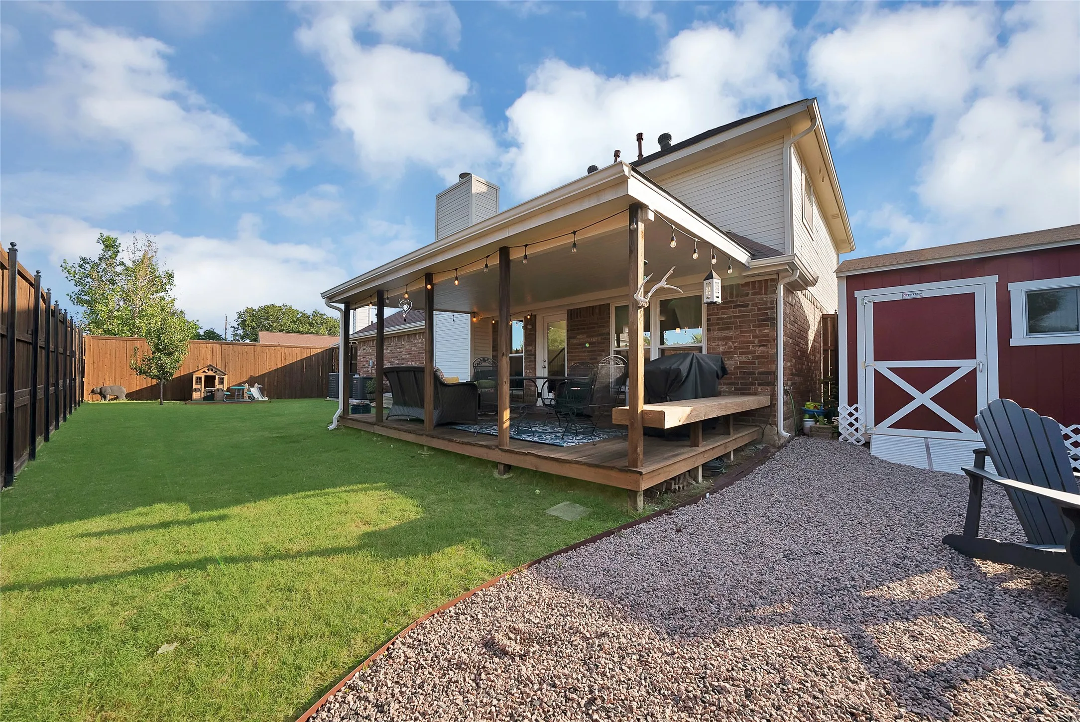 Expansive backyard featuring a covered patio, wood deck, large lawn, and a separate storage shed