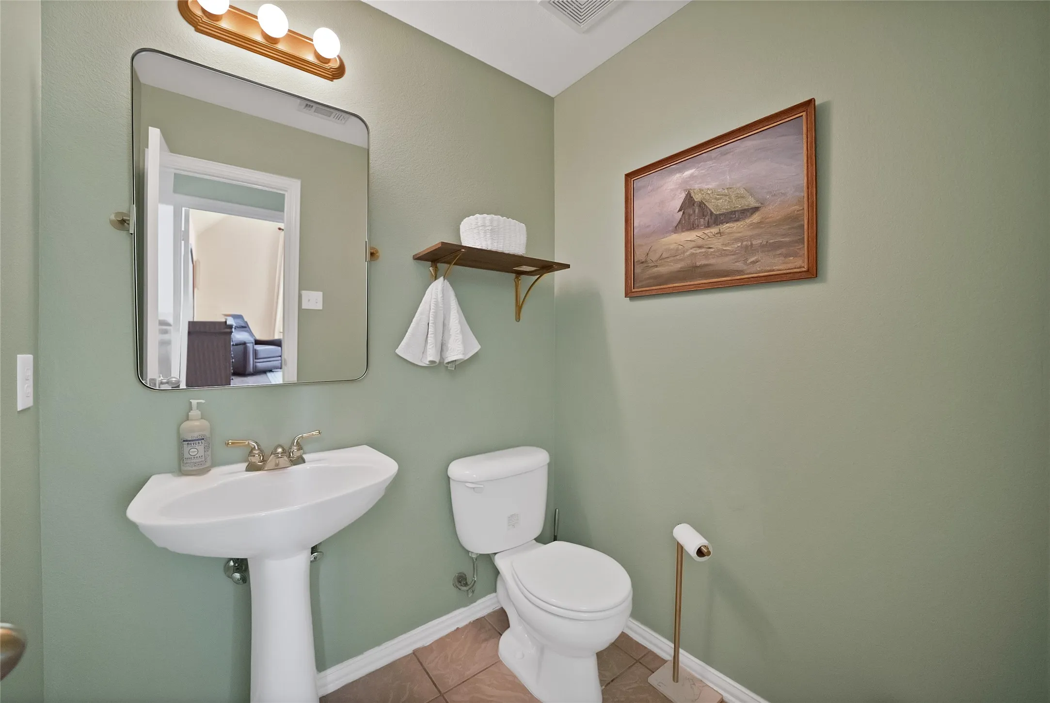 Pedestal sink with brass-finish faucet, rectangular wall-mounted mirror, and decorative wall shelf