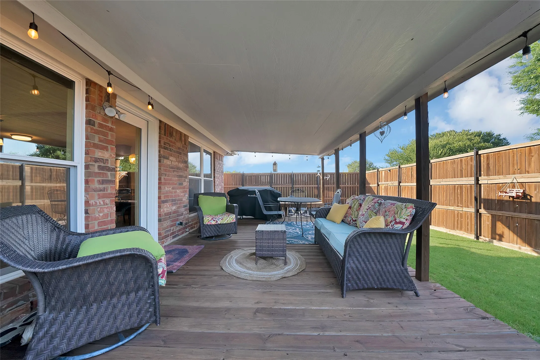 Expansive covered patio featuring wood decking, string lighting, and direct access to the interior