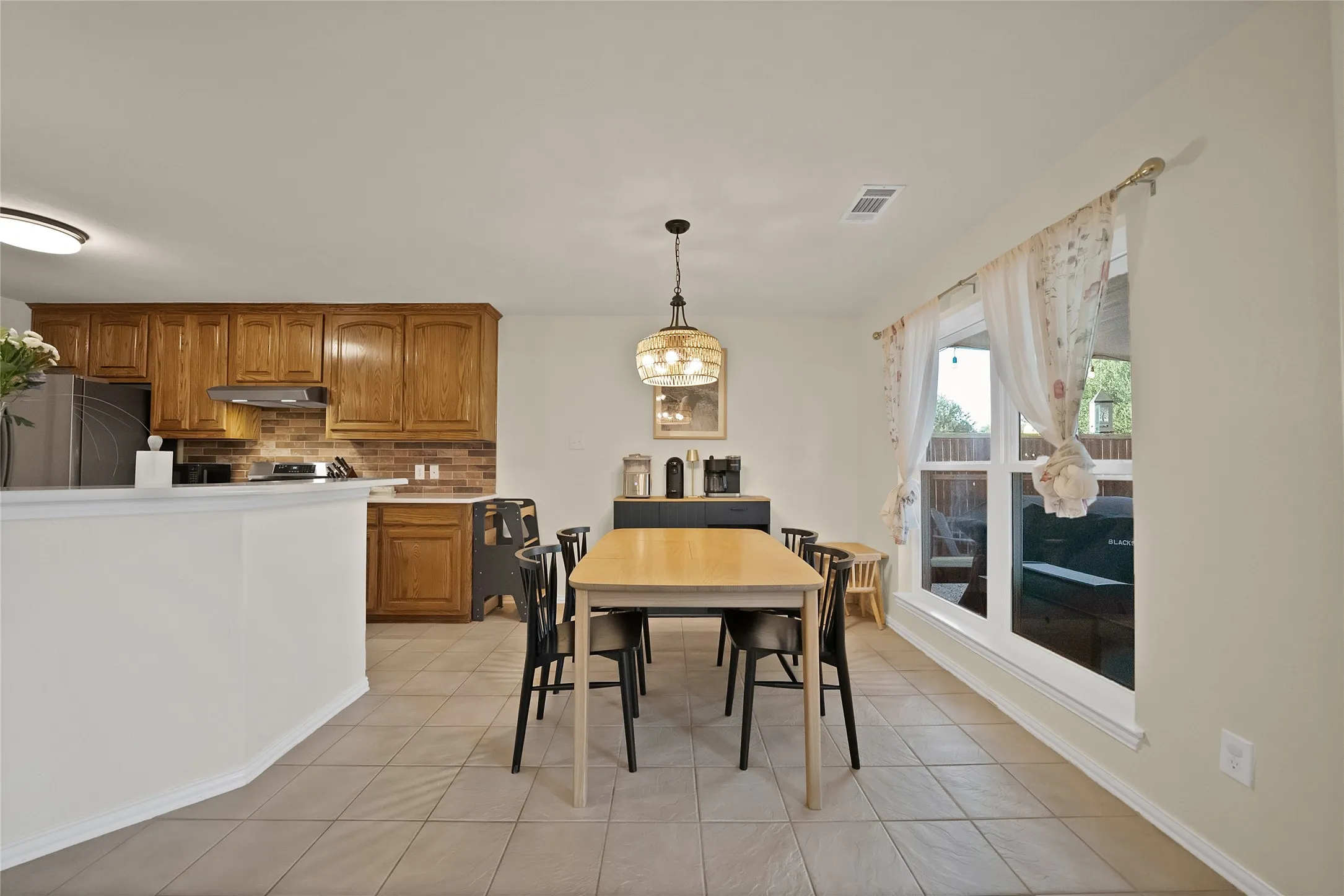 Dining area featuring tile flooring, a window with exterior views, and a kitchen pass-through with a breakfast bar