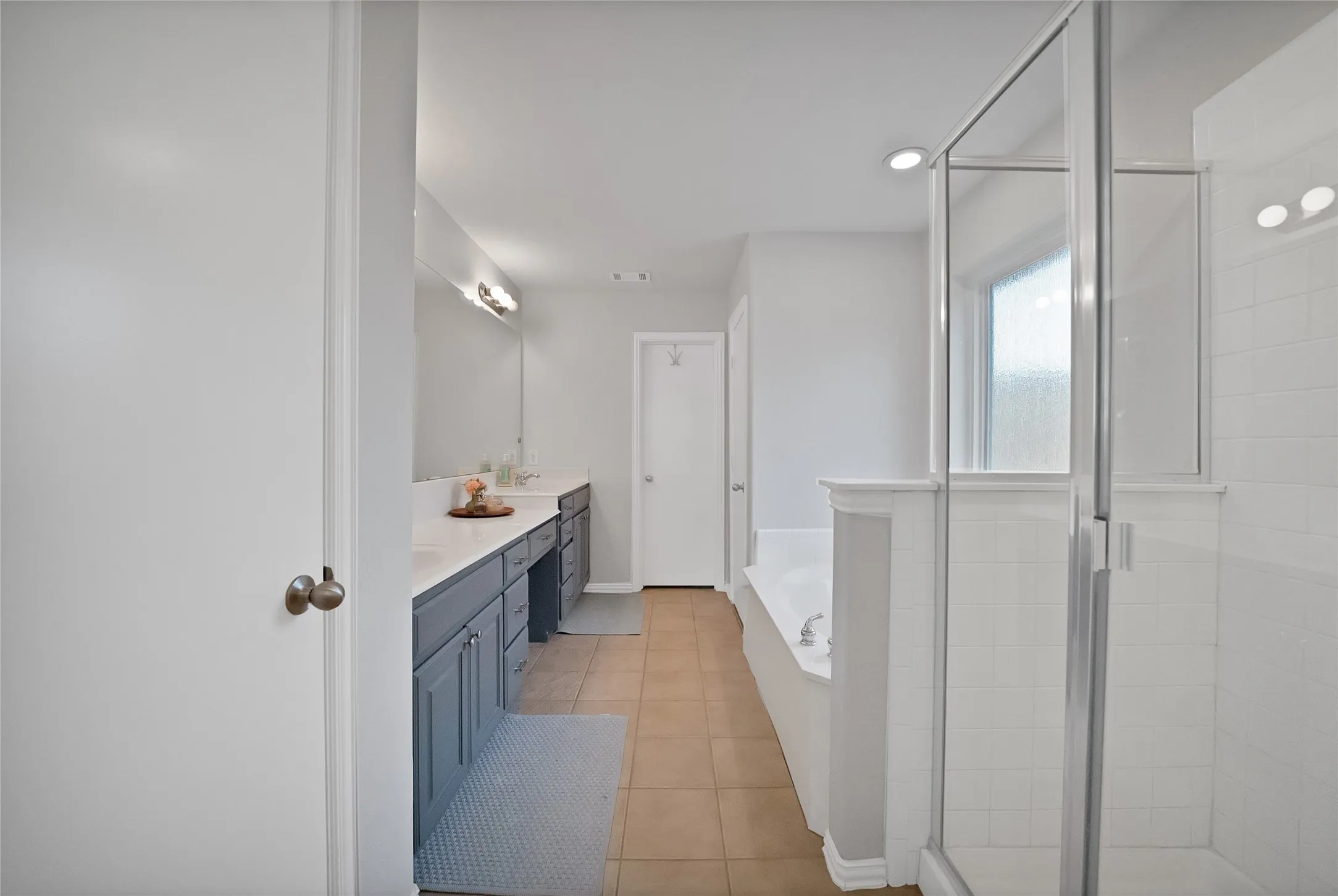 Bathroom featuring a glass-enclosed shower, built-in soaking tub, dual vanity with undermount sinks and white countertops, and neutral-toned tile flooring