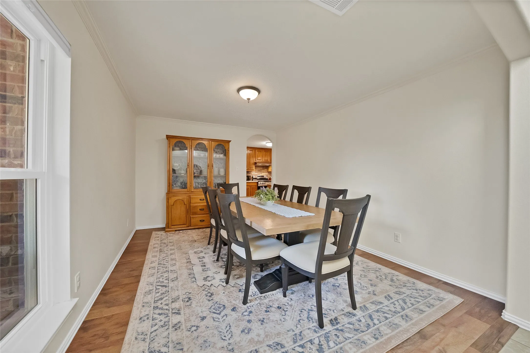 Spacious dining area featuring wood-finish flooring, white baseboards, and crown molding