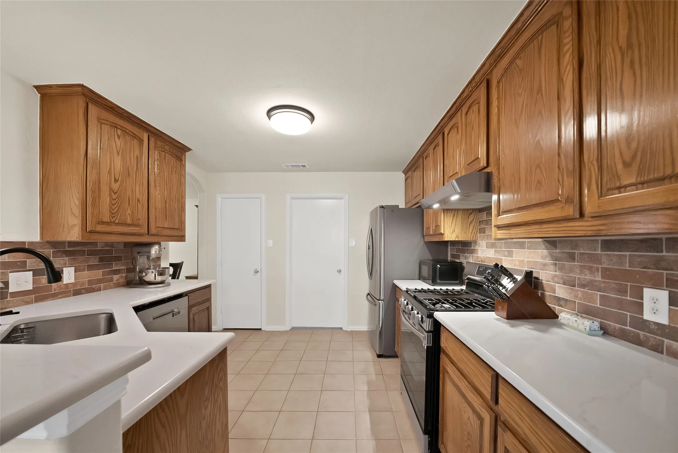 Kitchen featuring wood cabinetry, white countertops, tile flooring, and a brick-patterned tile backsplash