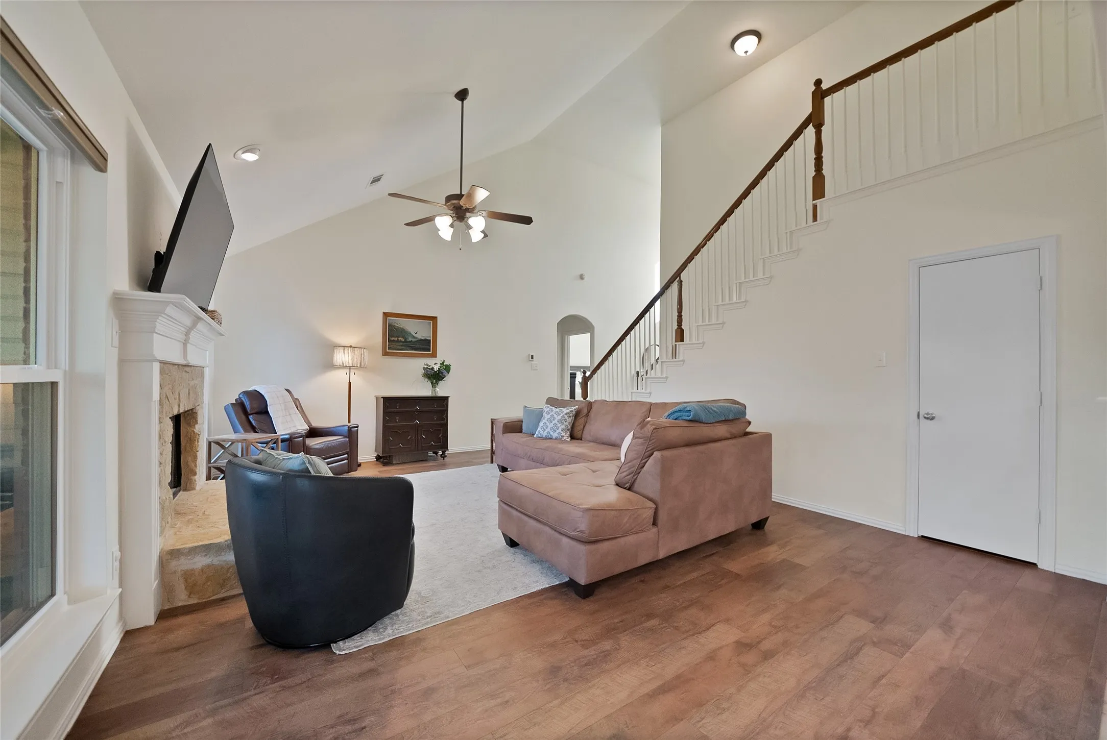 Living area featuring high vaulted ceilings, wood-finish flooring, and a stone fireplace with a white mantle