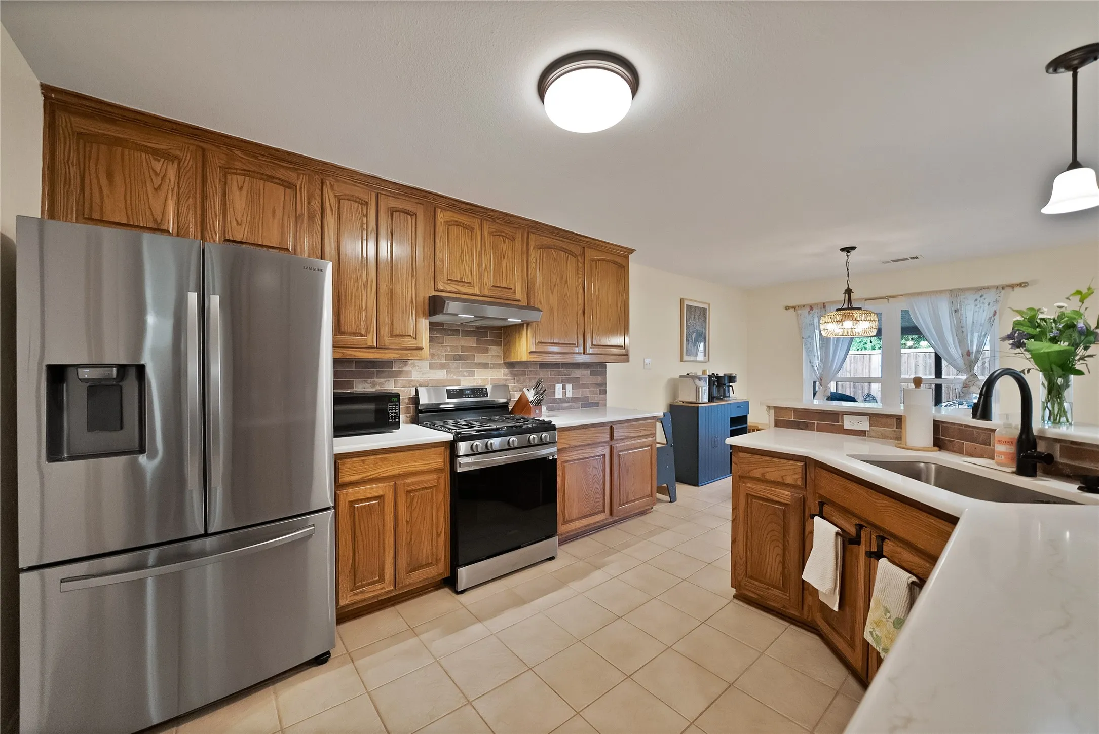 Kitchen featuring warm wood cabinetry, stainless steel appliances, a tile backsplash, and light-toned countertops