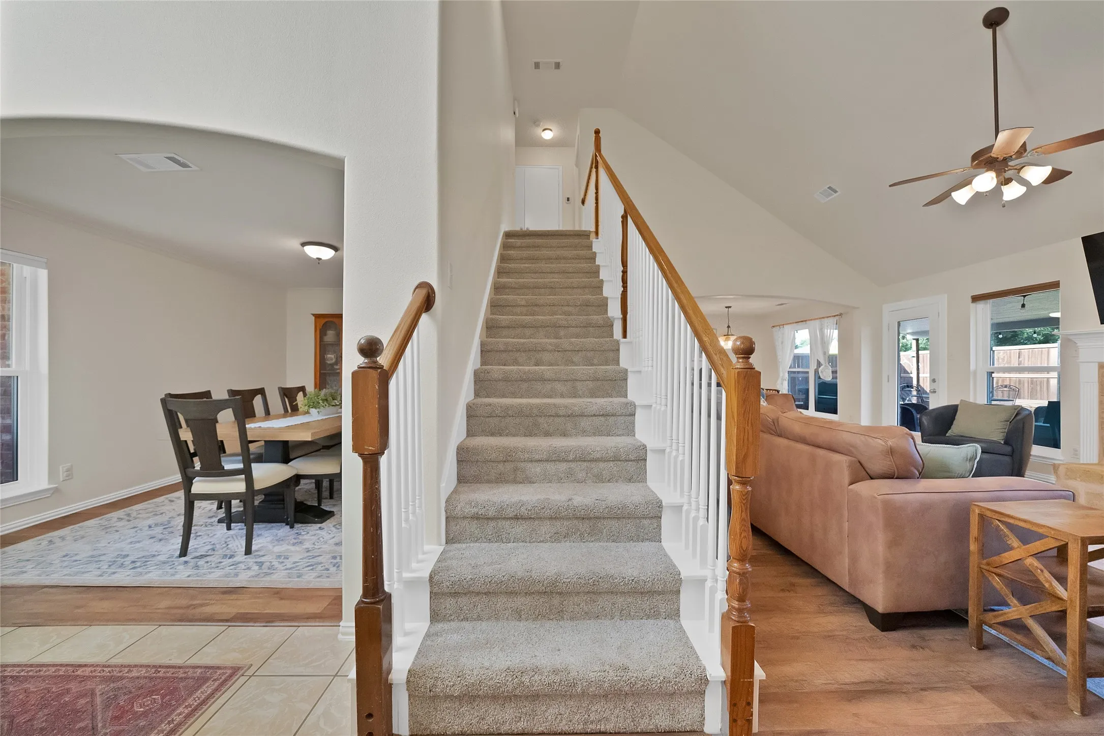Carpeted staircase with wood handrail and white spindles, hardwood-style flooring, vaulted ceiling, and arched entryway