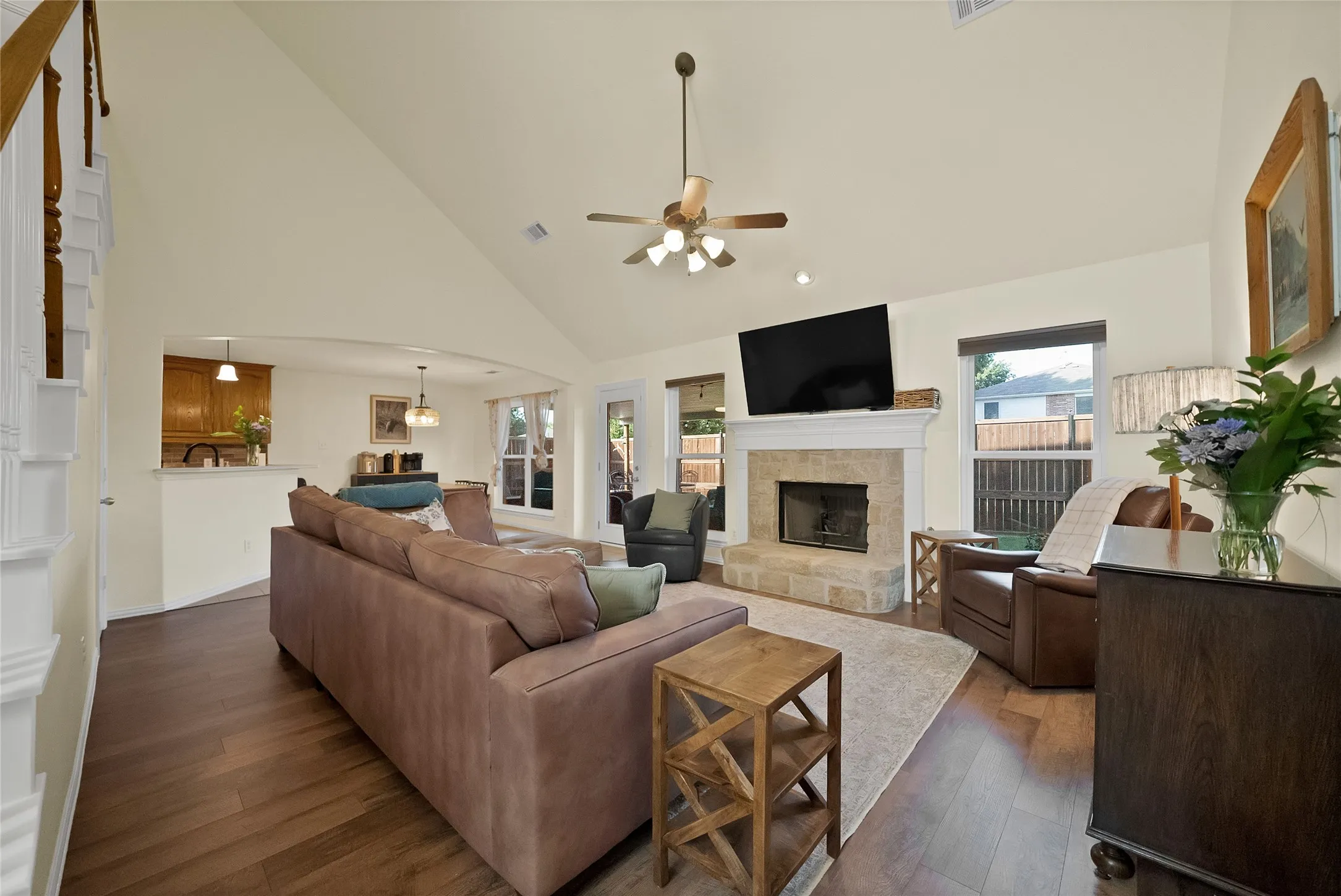 Spacious living area featuring high vaulted ceilings, wood-finish flooring, and a stone-clad fireplace with a white mantel