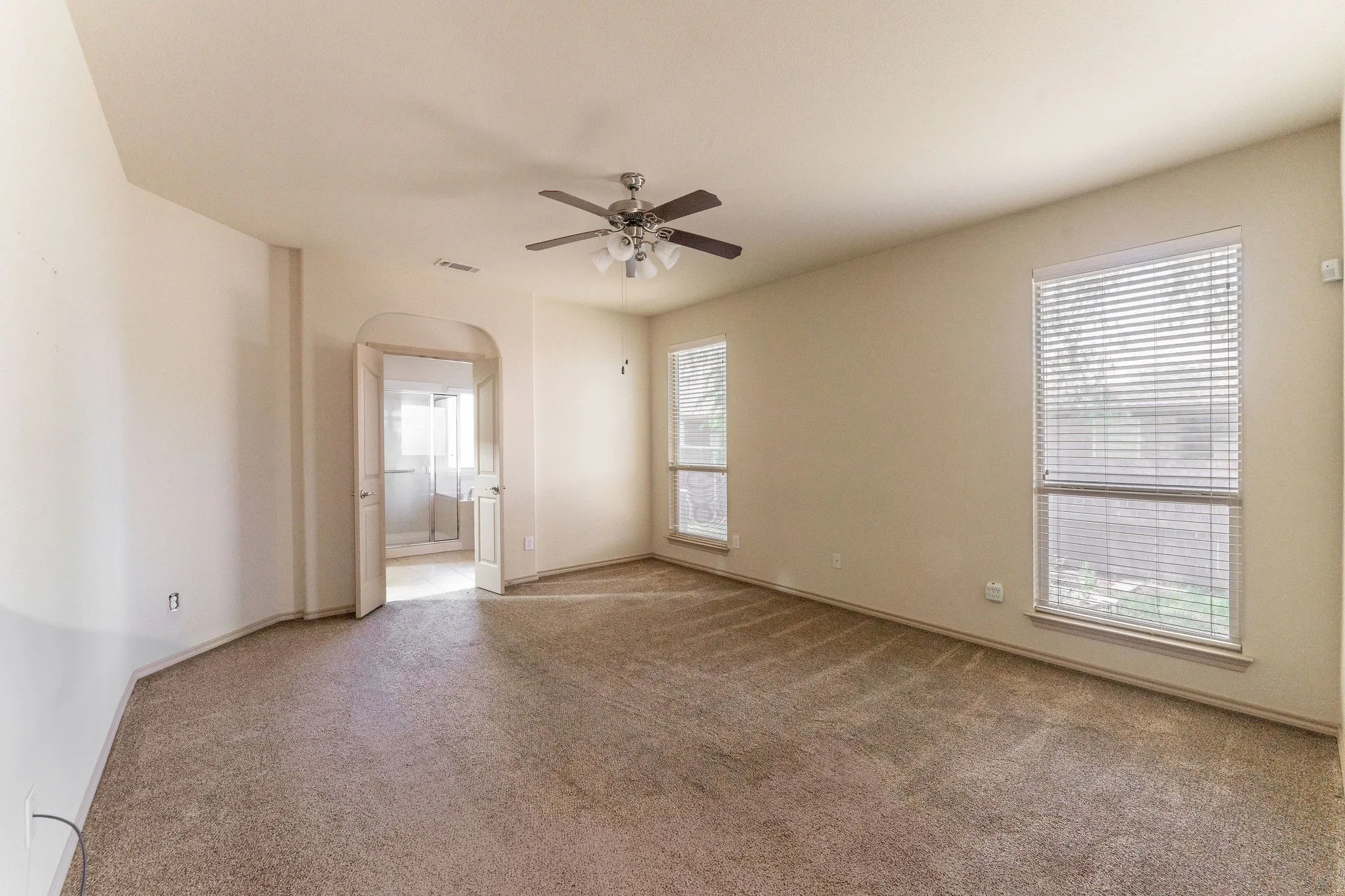 Spacious room featuring neutral carpeting, light-toned wall paint, and a ceiling fan with integrated lighting
