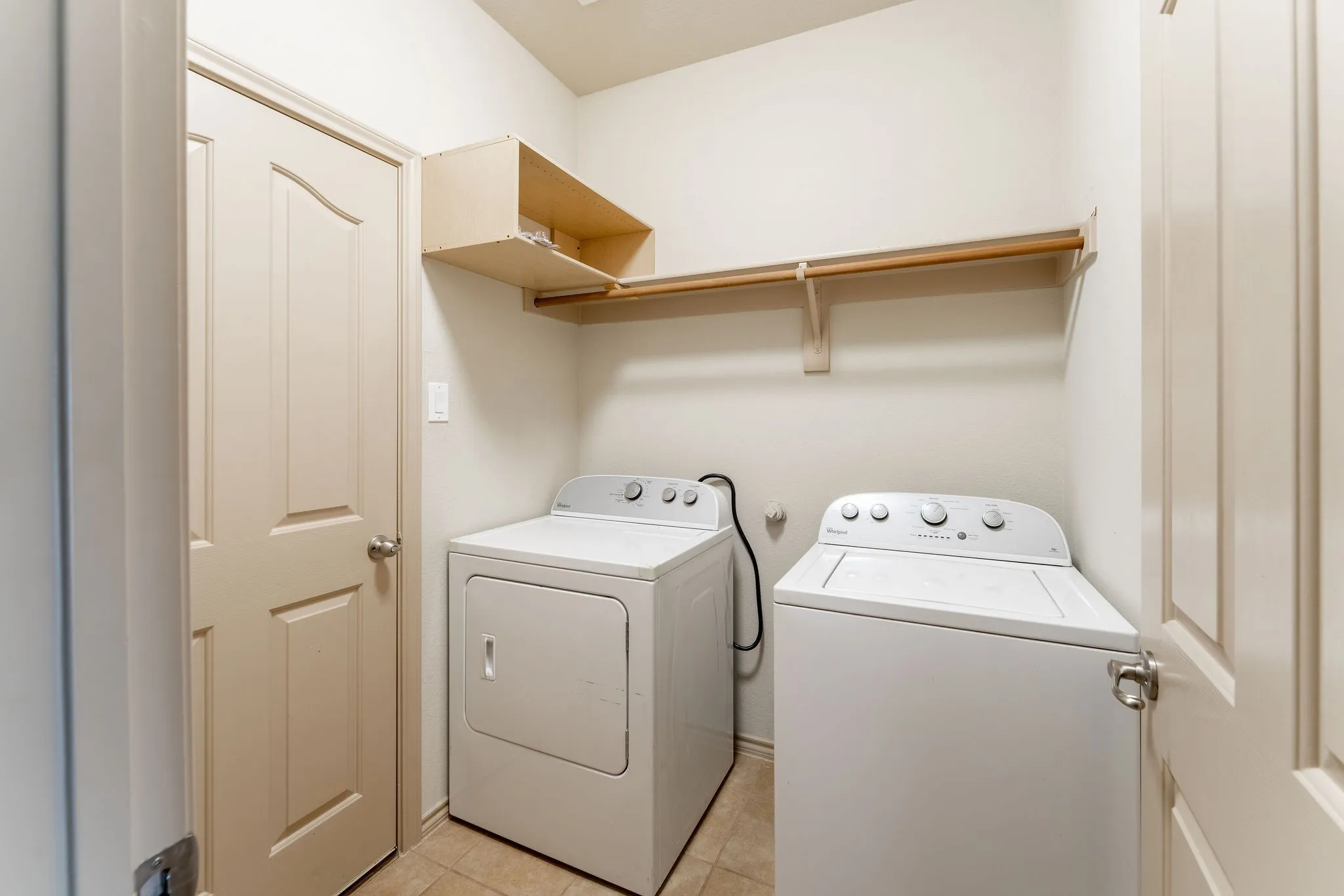 Utility space featuring light-colored panel doors, overhead shelving, and a clothing rod