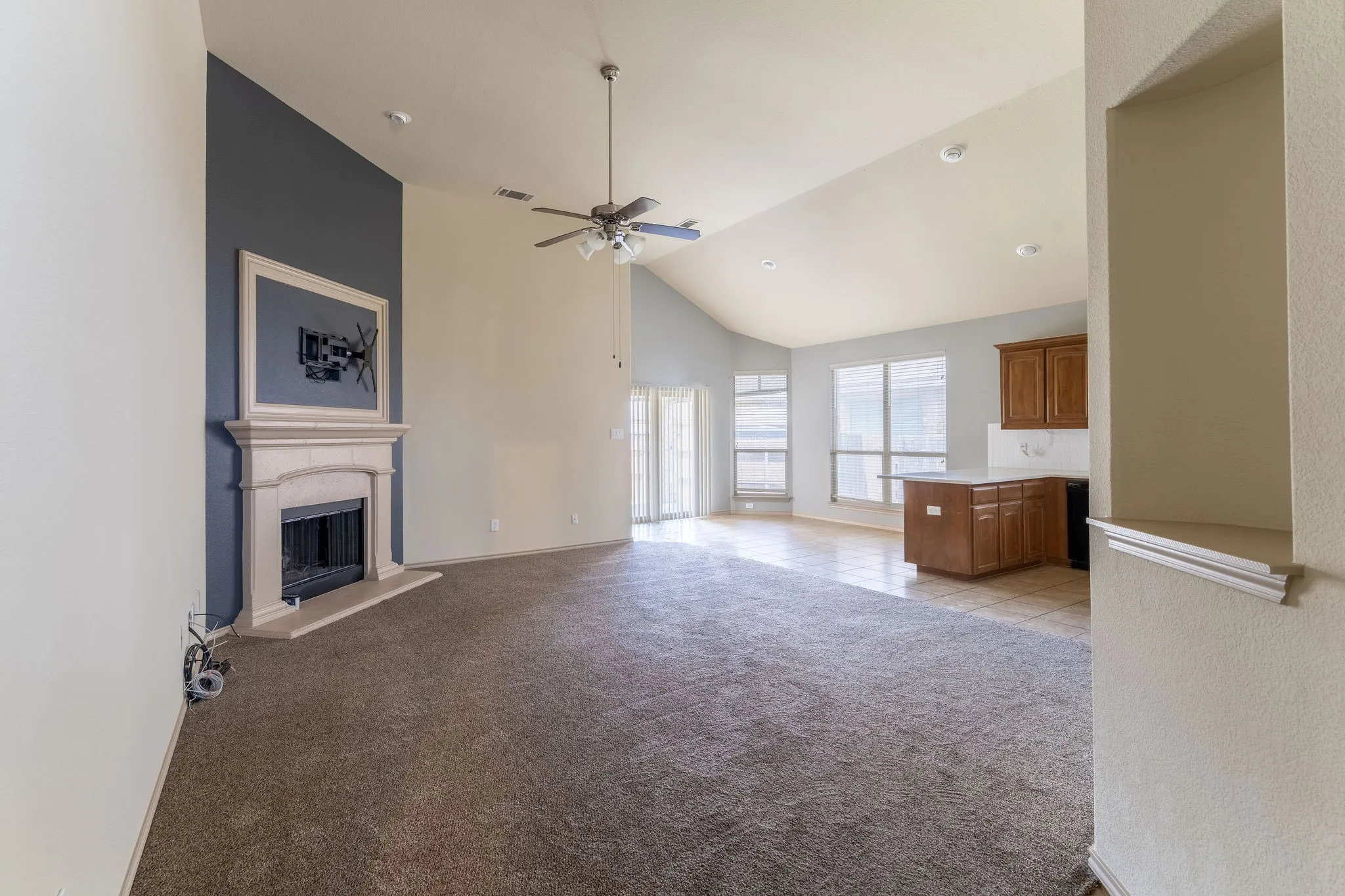 Spacious living area featuring a stone mantel fireplace, vaulted ceilings, and a ceiling fan