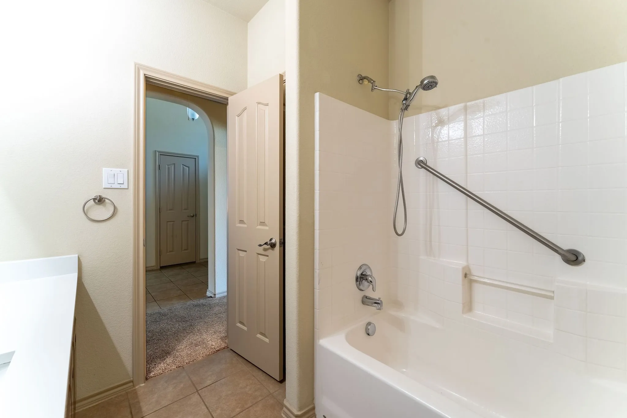 Bathroom featuring a white subway tile pattern, a built-in tub with grab bar, a chrome shower head with handheld sprayer, and a solid quartz surface countertop