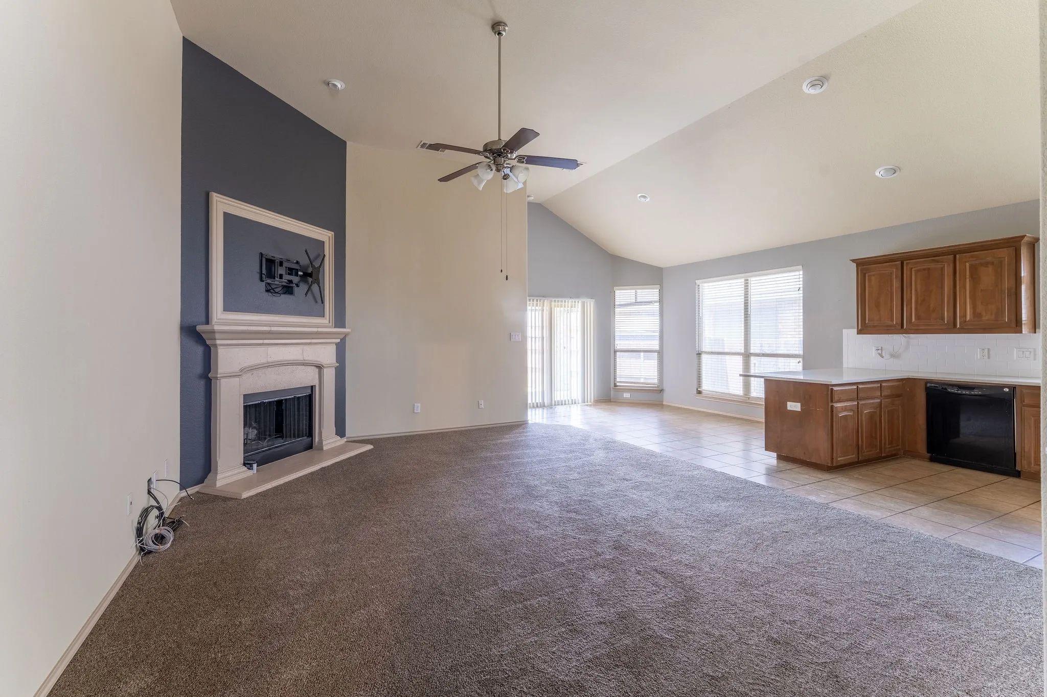 Open-concept living space featuring a vaulted ceiling and a stone-clad fireplace with a decorative mantel