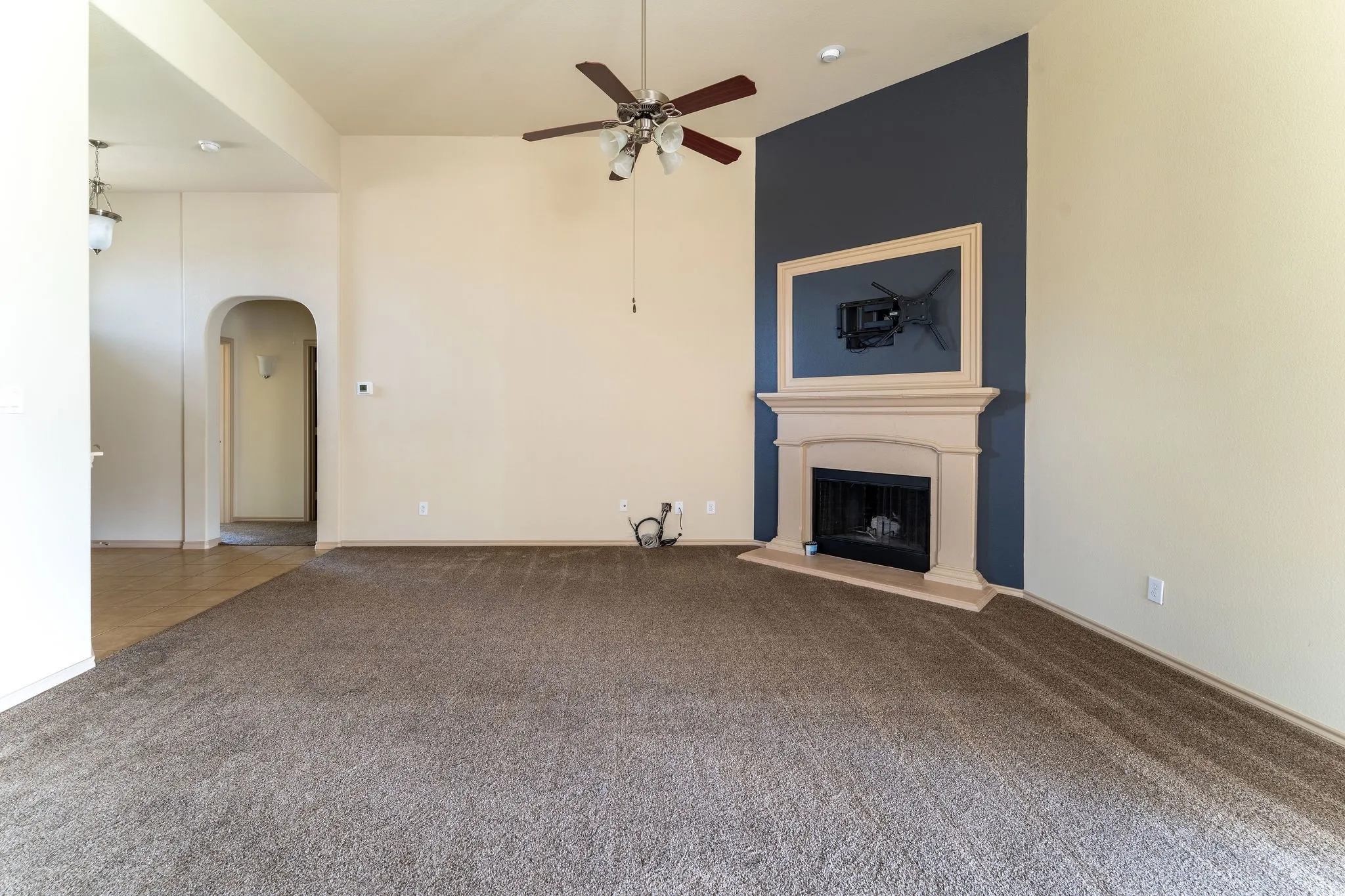 Spacious room with a fireplace featuring a decorative mantel, a ceiling fan, and carpet flooring