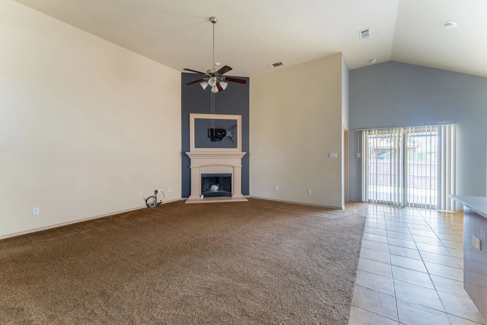 Living area featuring a fireplace with a light-toned mantelpiece, a ceiling fan, and vaulted ceilings