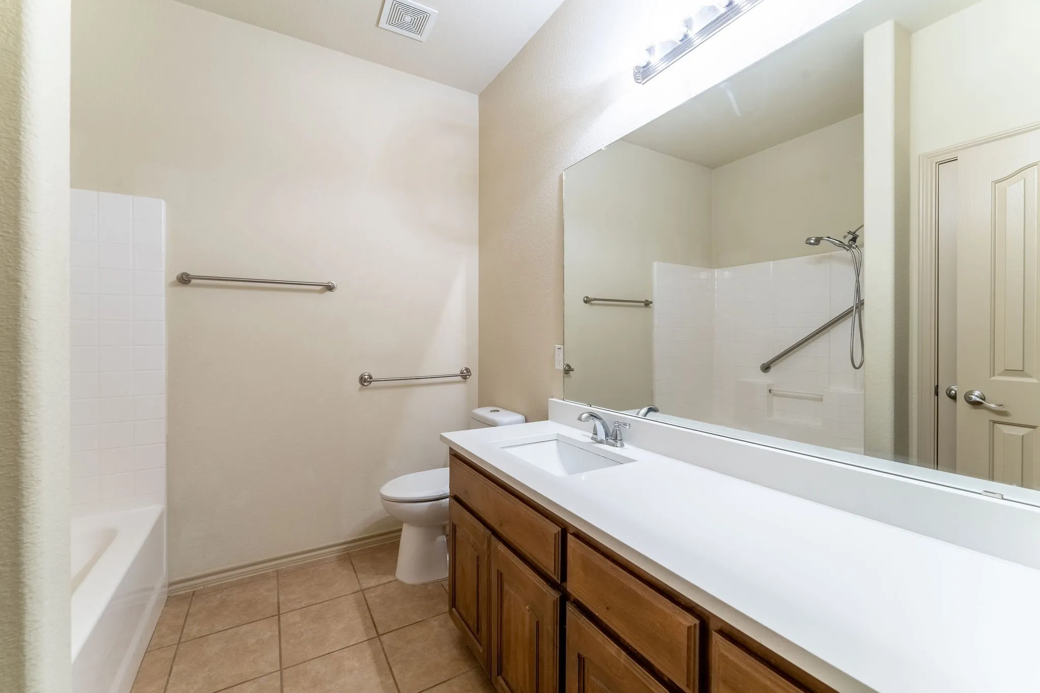 Bathroom featuring a wood-finish vanity with an integrated sink, a full-width mirror, tile flooring, and a tub/shower combination with grab bars
