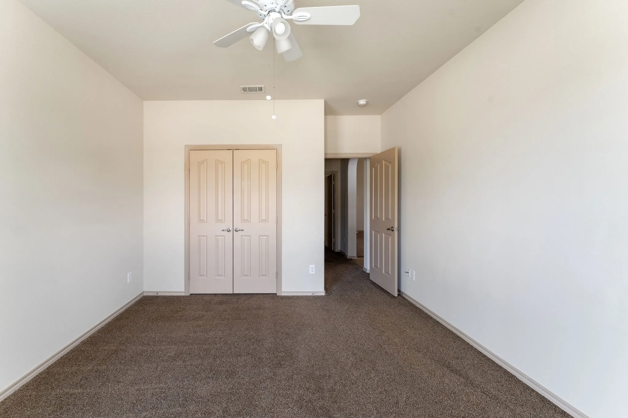 Spacious room featuring neutral carpeting, light-toned walls, and a ceiling fan with integrated lighting