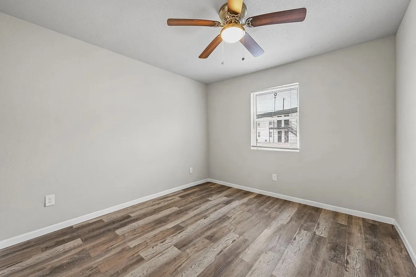 Room featuring wood-finish flooring, light gray walls, a ceiling fan with integrated lighting, and a single window with blinds